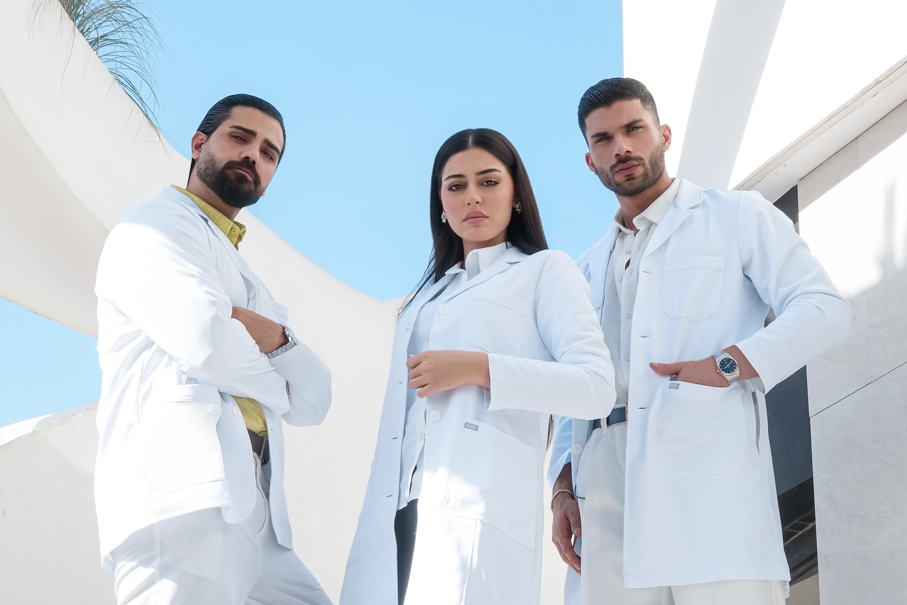 Three individuals in white lab coats standing outdoors with a clear blue sky.