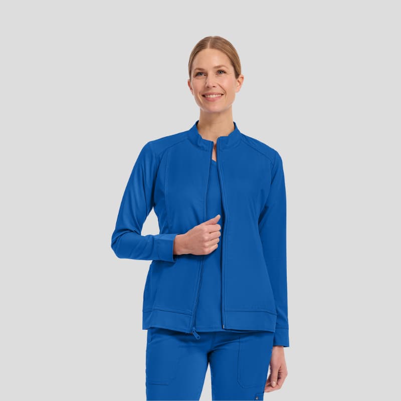 Smiling woman wearing blue medical scrub jacket and matching pants on light background