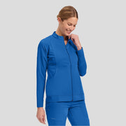 Woman wearing blue zip-up medical scrub jacket and matching scrub pants on grey background